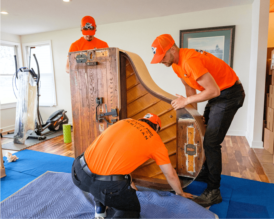 Professional movers carefully wrapping and moving a piano